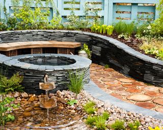 curved slate garden wall with water feature surrounded by beds mulched with wood chips