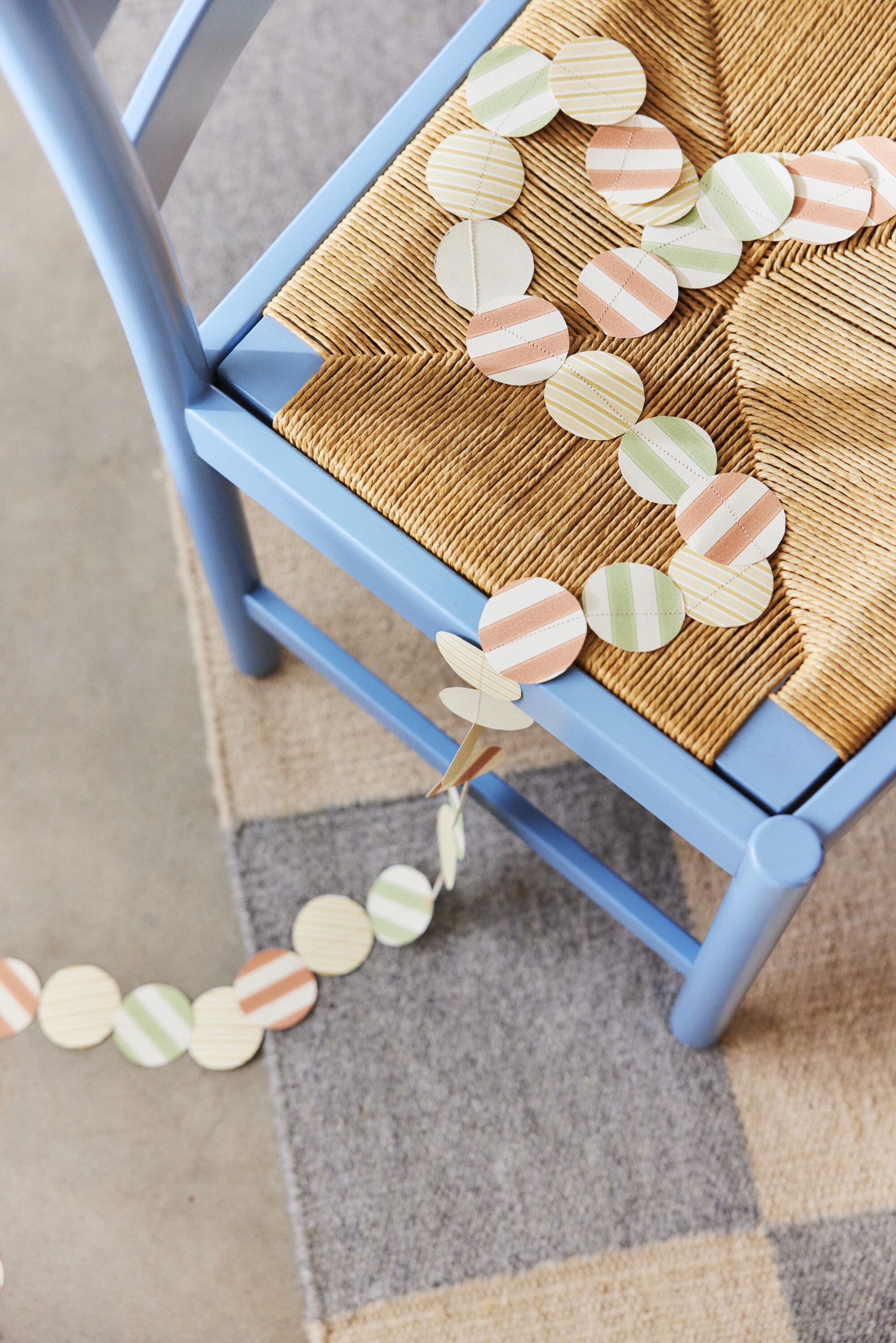 Image of a light blue and wicker dining chair with a garland of wallpaper circles draped on top of it