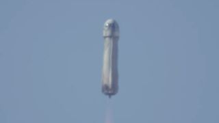 a white rocket lifts off above a desert full of scrub plants