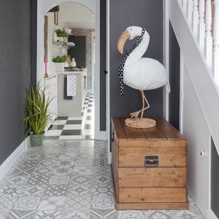 Grey hallway with geo style floor tiles and a stork statue on a wooden cabinet