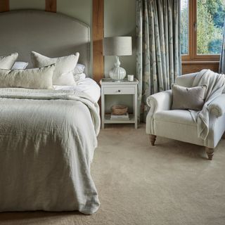 A guest bedroom in a neutral colour scheme with a curved fabric headboard and linen bed linen