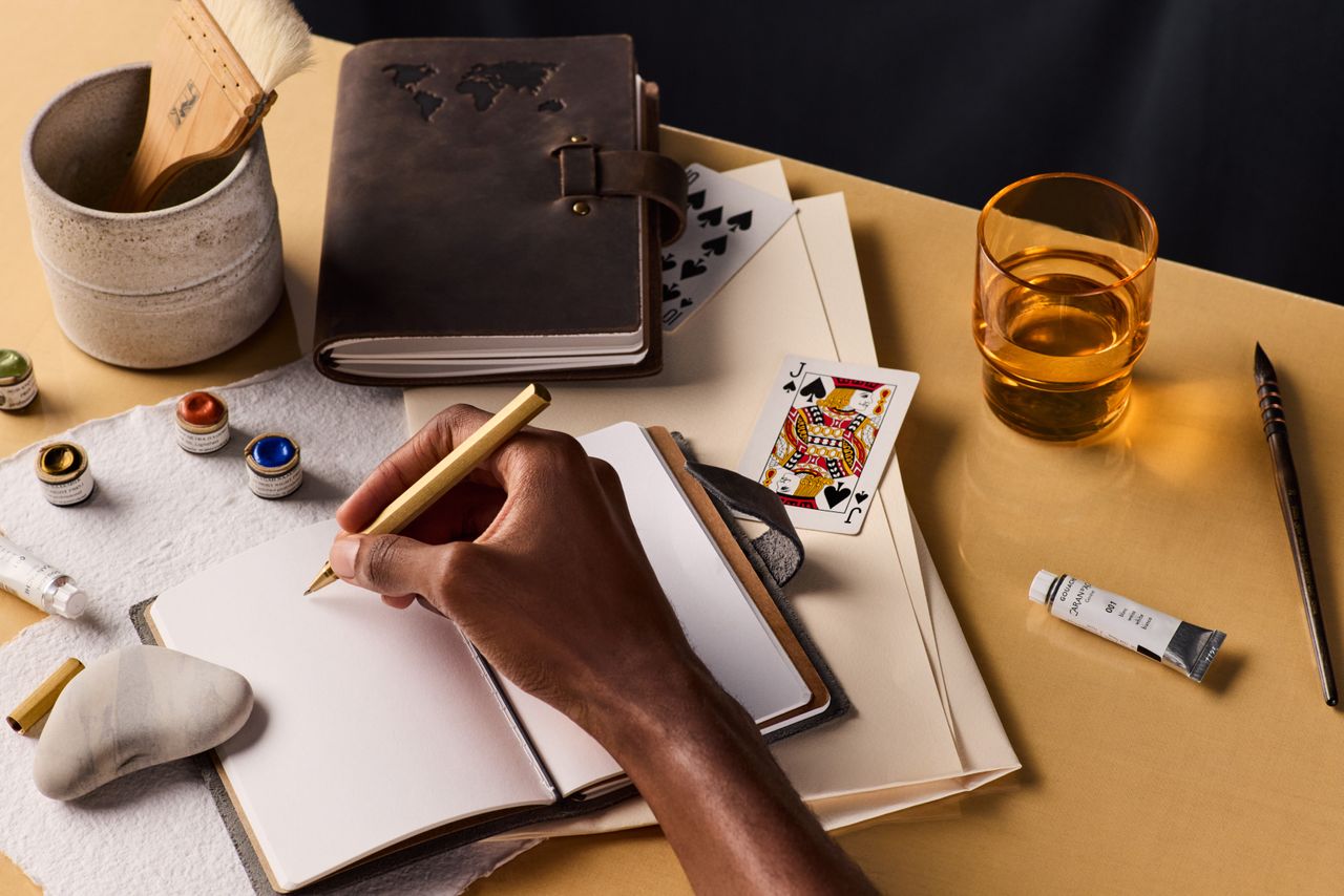 Person&#039;s hand holding pen, ready to write in open travel journal