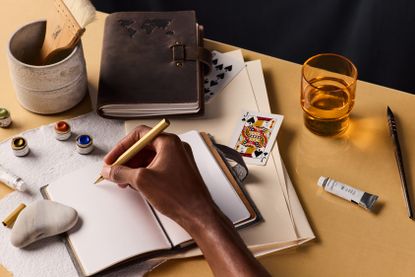 Person's hand holding pen, ready to write in open travel journal