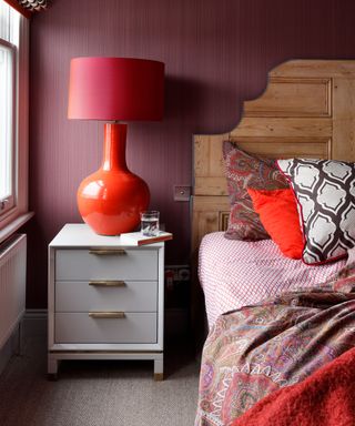 An example of guest bedroom ideas showing a maroon wall behind a bed with a wooden headboard