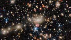 An image of deep space, where blue, red and orange stars twinkle next to golden and orange galaxies. 