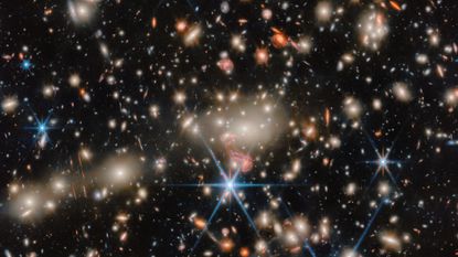 An image of deep space, where blue, red and orange stars twinkle next to golden and orange galaxies. 