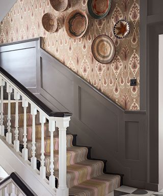 carpeted staircase with painted grey wooden panelling and patterned wallpaper in a natural color palette, decorative wall hangings