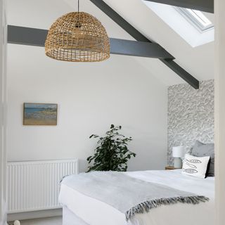 White bedroom with a bed and cushions and large hanging wicker light