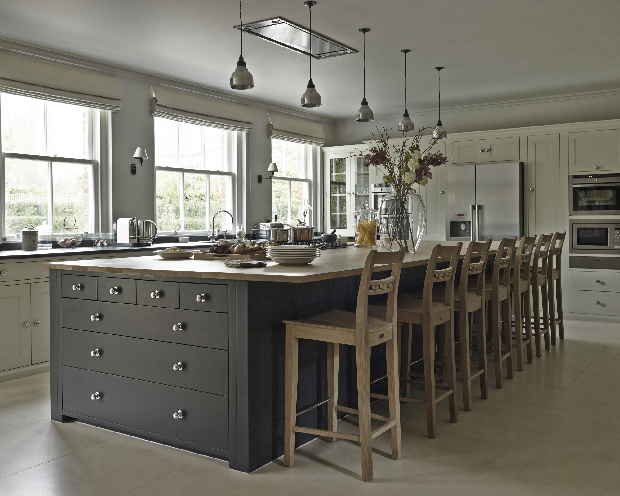 A long gray painted kitchen island with a row of wooden chairs in a traditional kitchen scheme.