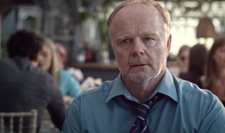 Jason Watkins as Ed in the catch, wearing a shirt and tie and sitting in a restaurant.