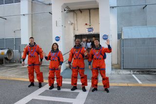 four humans waving on Earth with orange spacesuits.