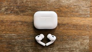 Helt trådløse ørepropper av typen AirPods Pro 2 avbildet sammen med det tilhørende etuiet på en bordplate av tre.