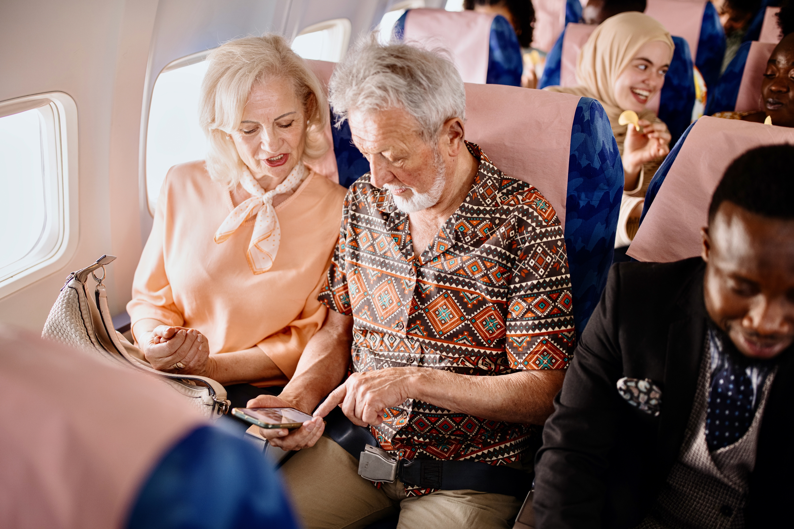 A mature couple seated on an airplane look at a phone together. 