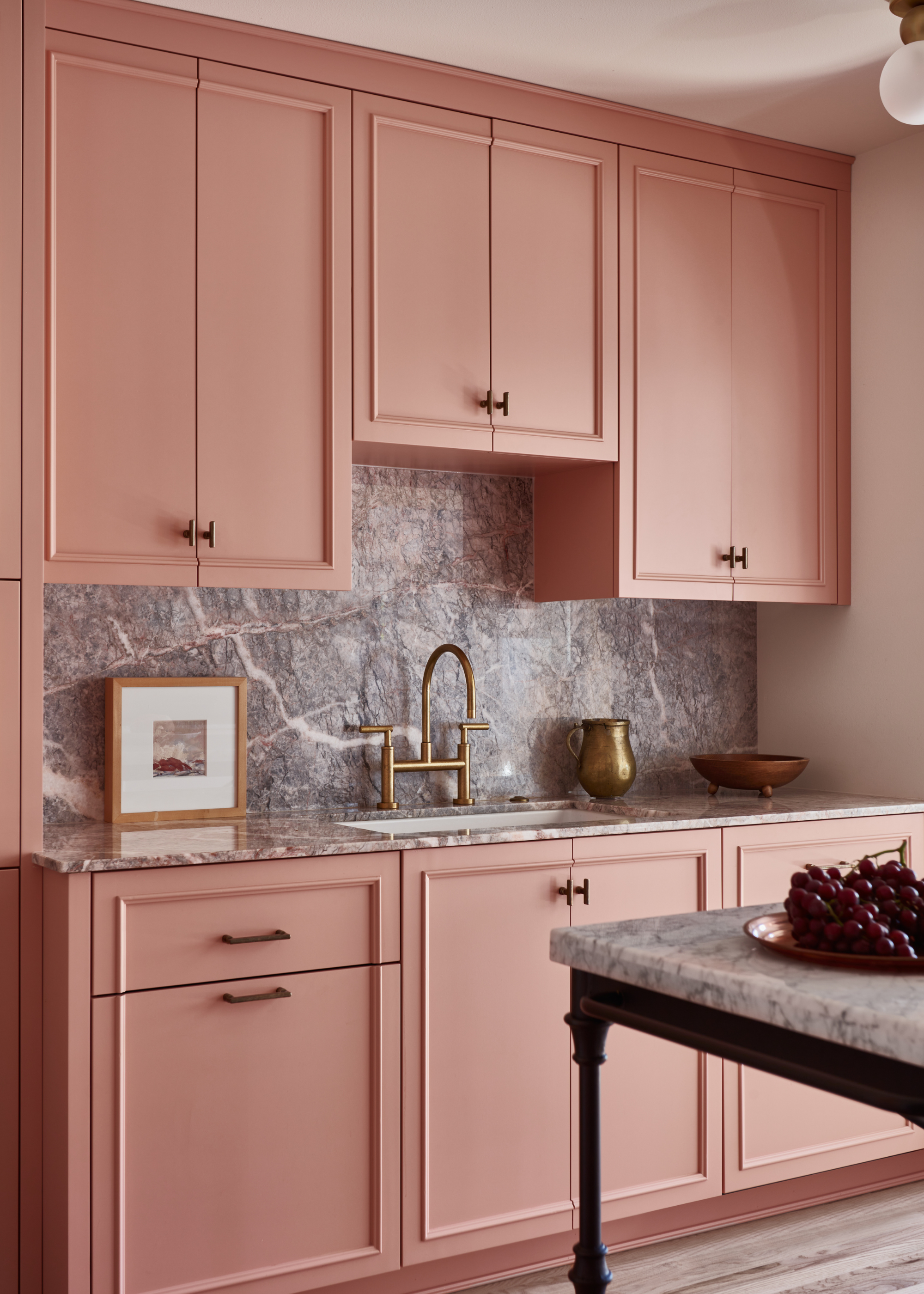 A pink kitchen with ceiling height wall cabinets and gray marble countertop and backsplash