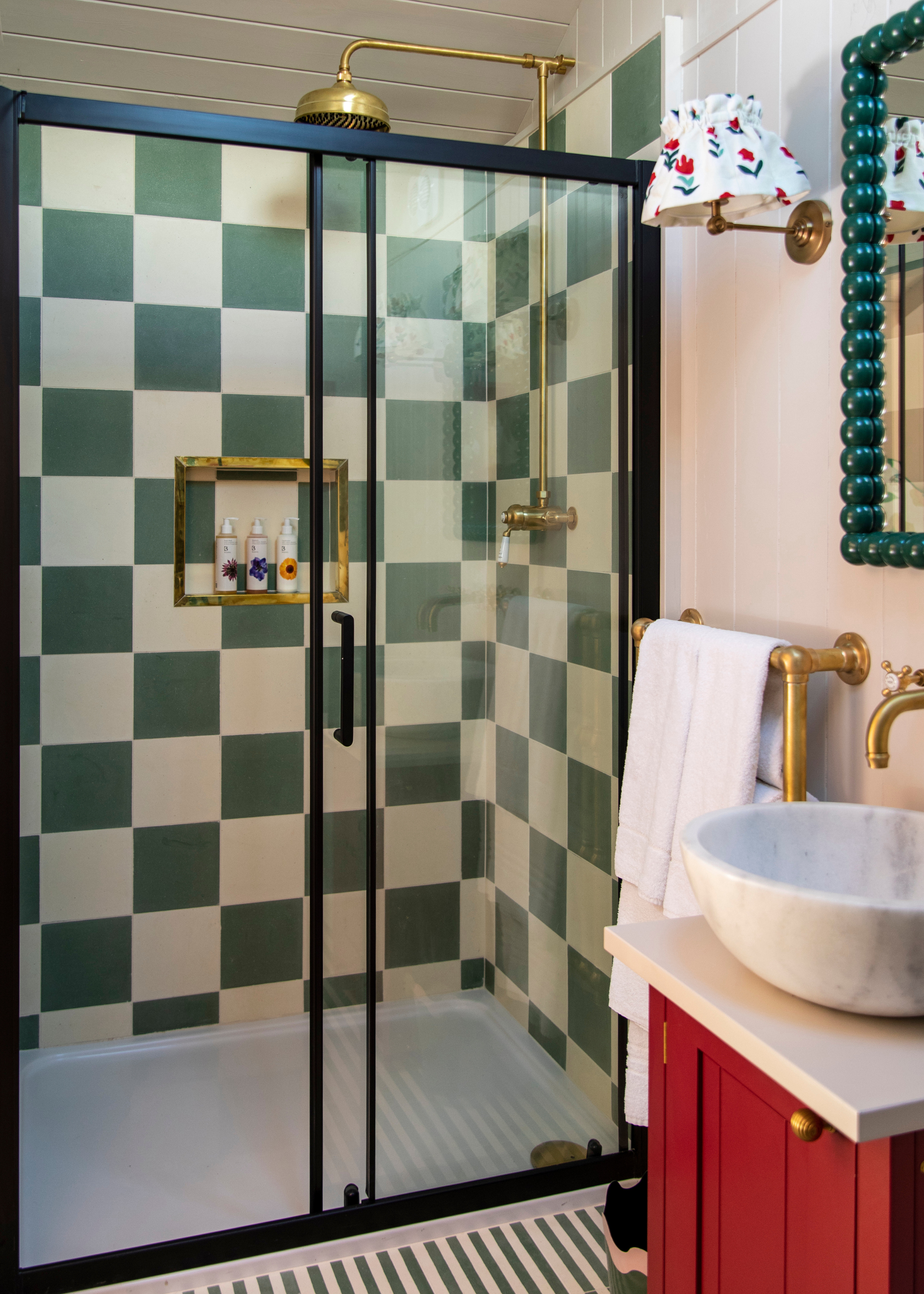 checkerboard tiled shower with doors and a red cabinet with a sink on top