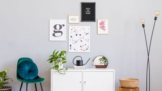 Gallery wall on a pale grey/ white background with different frames and pictures hung on the wall over a cupboard unit