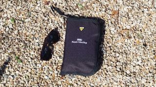 A folded bike cover in a pouch on the floor next to some sunglasses