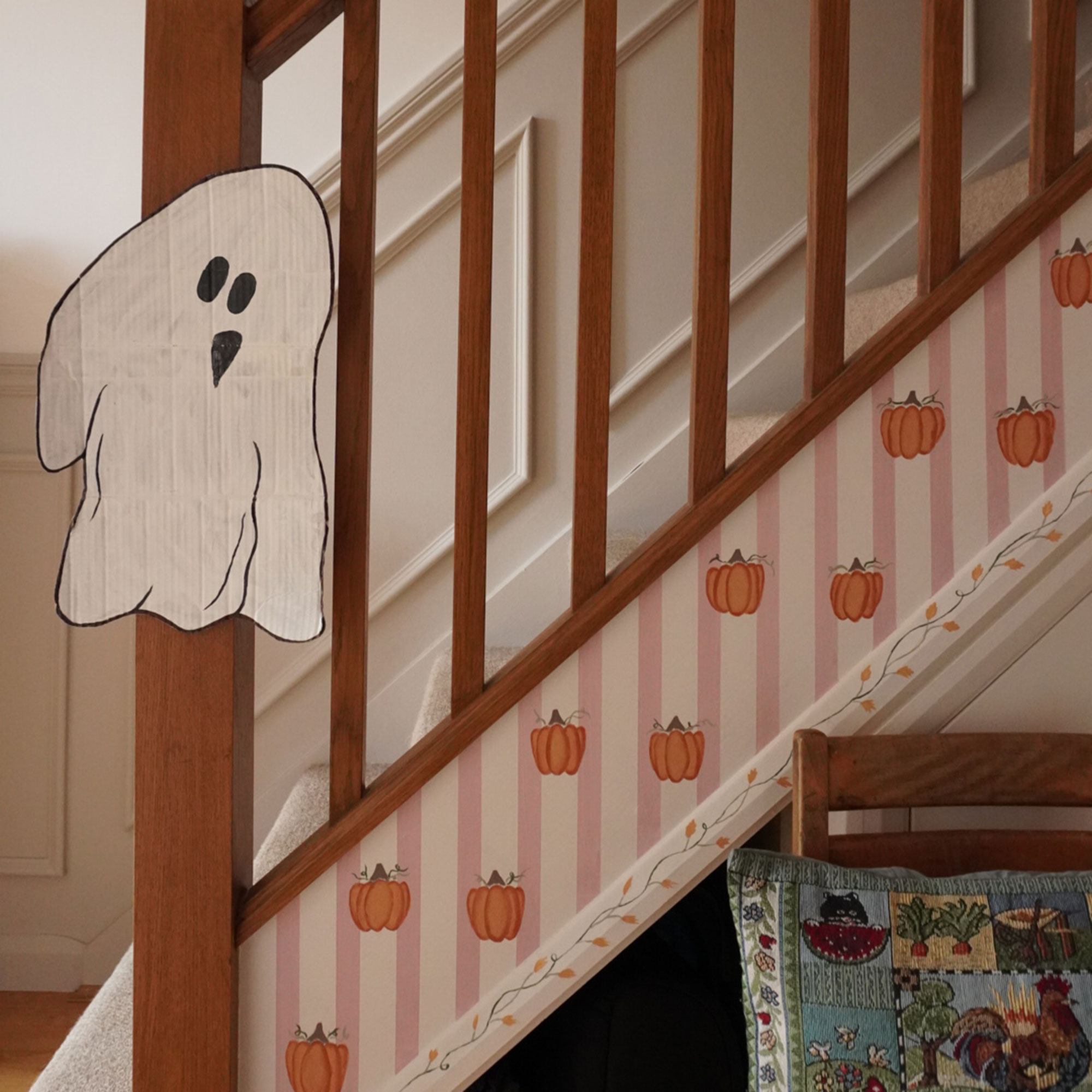 Staircase with pumpkin mural painted up the sideboard and cardboard ghost cut out attached to banister pole