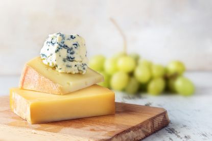 Our healthiest cheese list includes blue and hard cheeses stacked on a chopping board here.