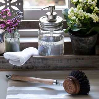 mason jar pump wih liquid soap wooden dish brush and jar with flowers