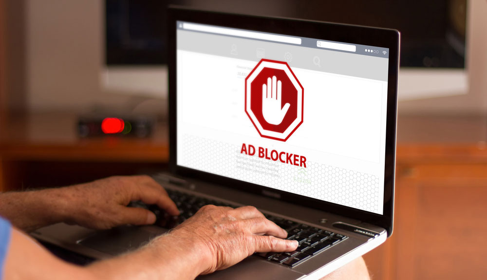 Die Hände eines Mannes tippen auf einem Laptop, auf dem die Worte „Werbeblocker“ angezeigt werden.