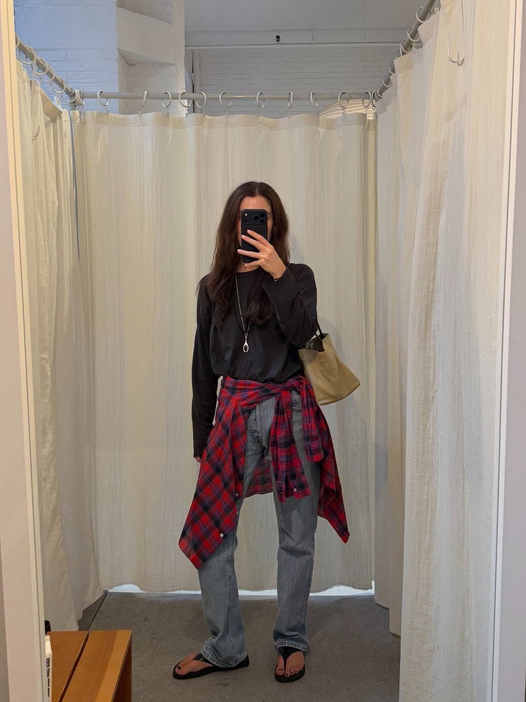 annabelrosendahl shows how to wear a plaid shirt in 2026. She wears a loose black top, a red shirt around the waist, straight-leg jeans and flip flops.