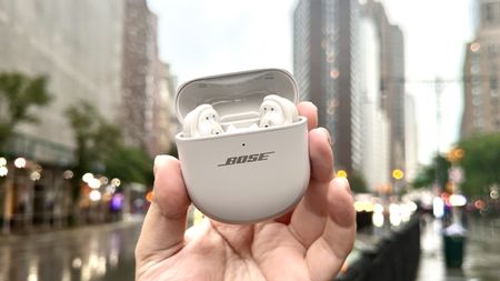 Someone holding the Bose QuietComfort Ultra Earbuds while outside