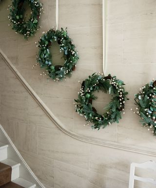 Christmas stair decor ideas with four green wreaths hung on a cream staircase wall