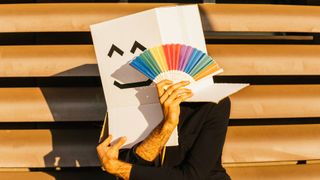 Businessman wearing box with smiley face holding rainbow color hand fan - stock photo