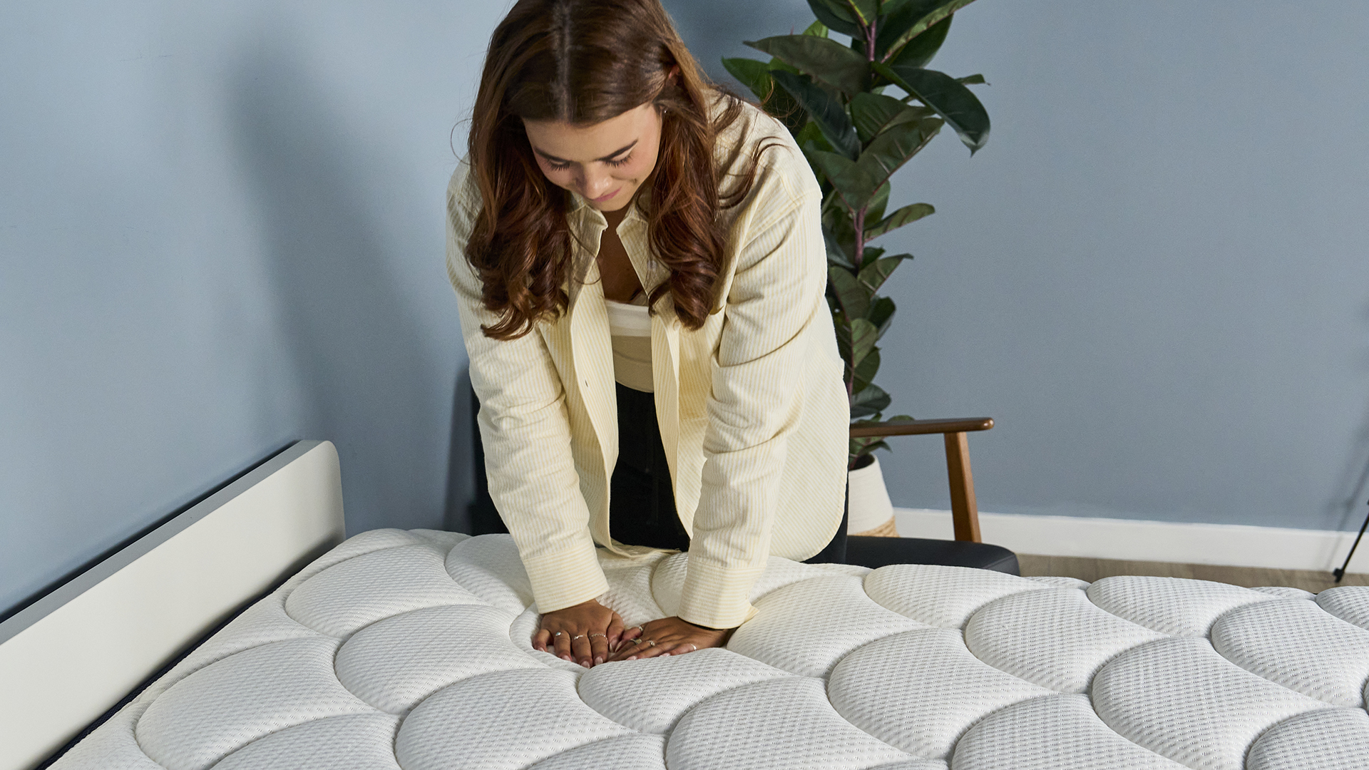 This image shows our mattress tester Eve Davies using both hands to press into the surface of the DreamCloud Classic Hybrid Mattress on a bed frame in our Sleep Lab, to test the support and comfort