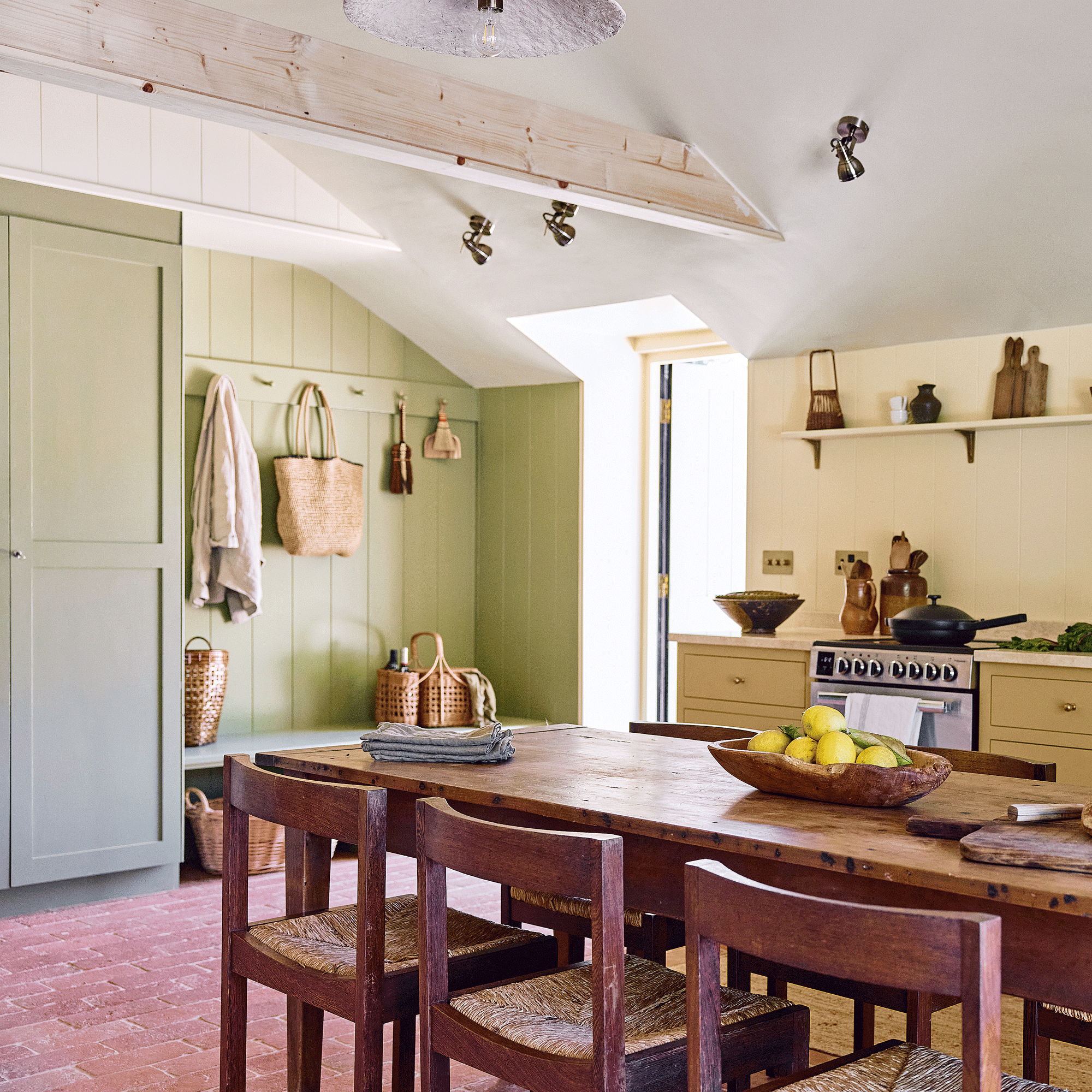 an open plan kitchen diner with a green boot room area, yellow kitchen area and an old reclaimed table and chairs