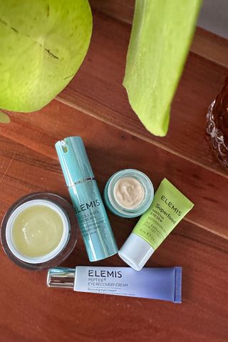 An array of Elemis eye cream shot on a wooden side table with a plant