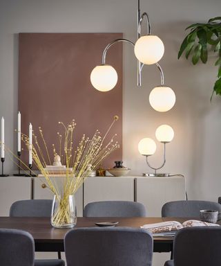 IKEA dining room with chrome globe lighting and pink artwork with gray chairs and wooden dining table