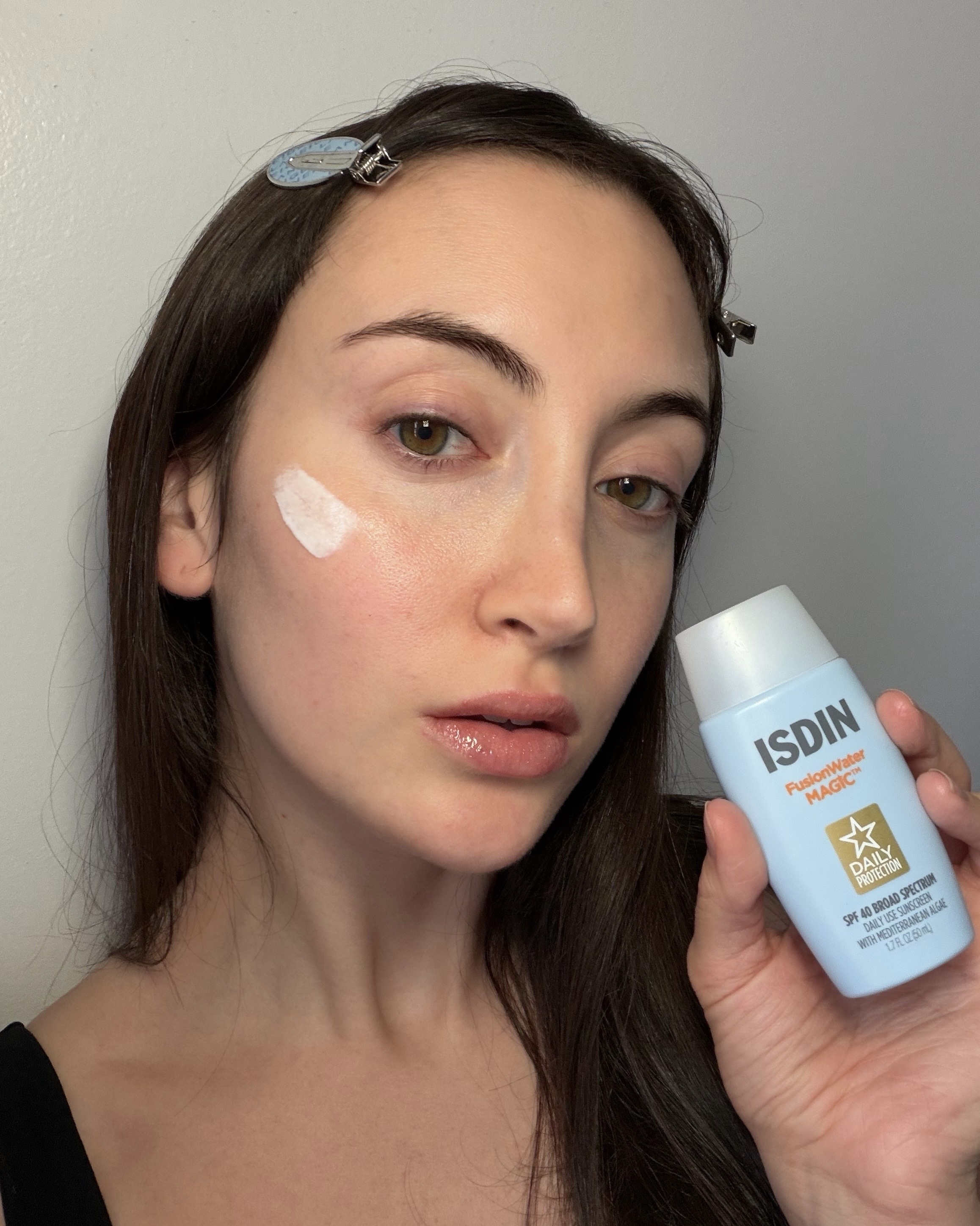 An image of Who What Wear associate beauty editor Alyssa Brascia wearing and holding the Isdin Fusion Water Magic sunscreen.