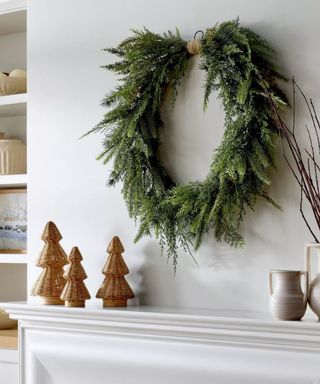 Christmas mantle with large wreath hanging above and three wicker Christmas trees