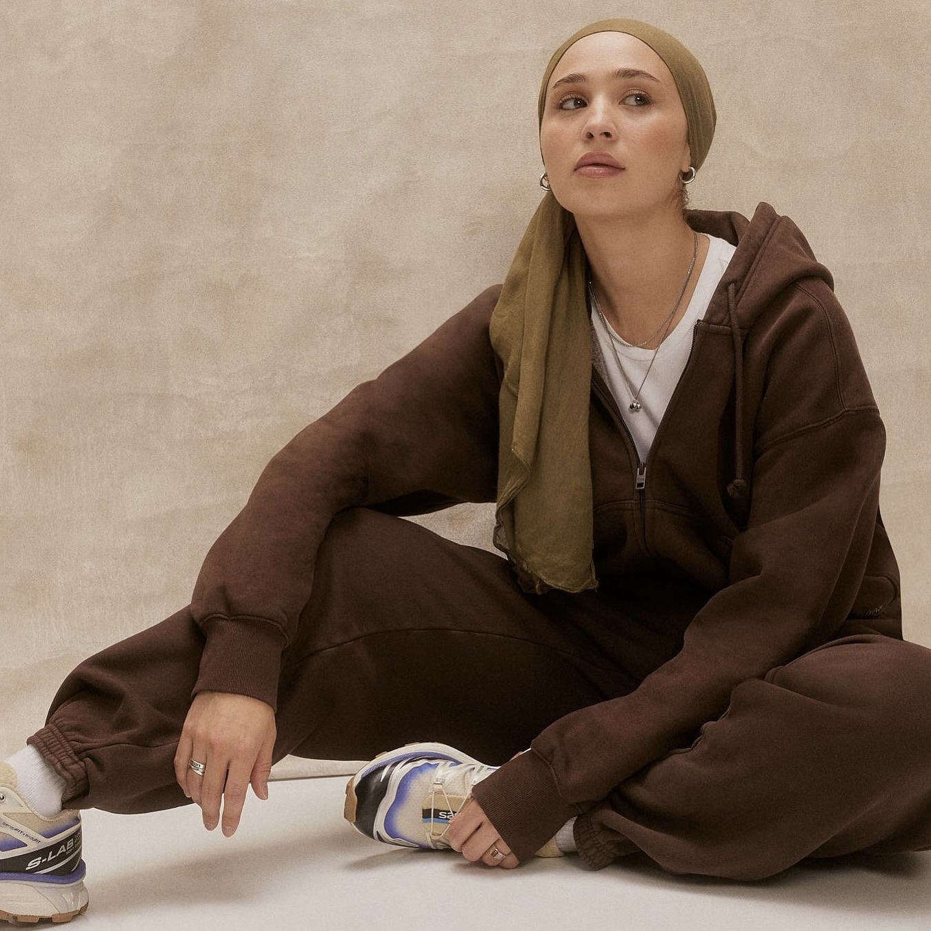 maria alia wearing a brown lounge set with a white tee, salomon sneakers, and an olive headscarf&nbsp;