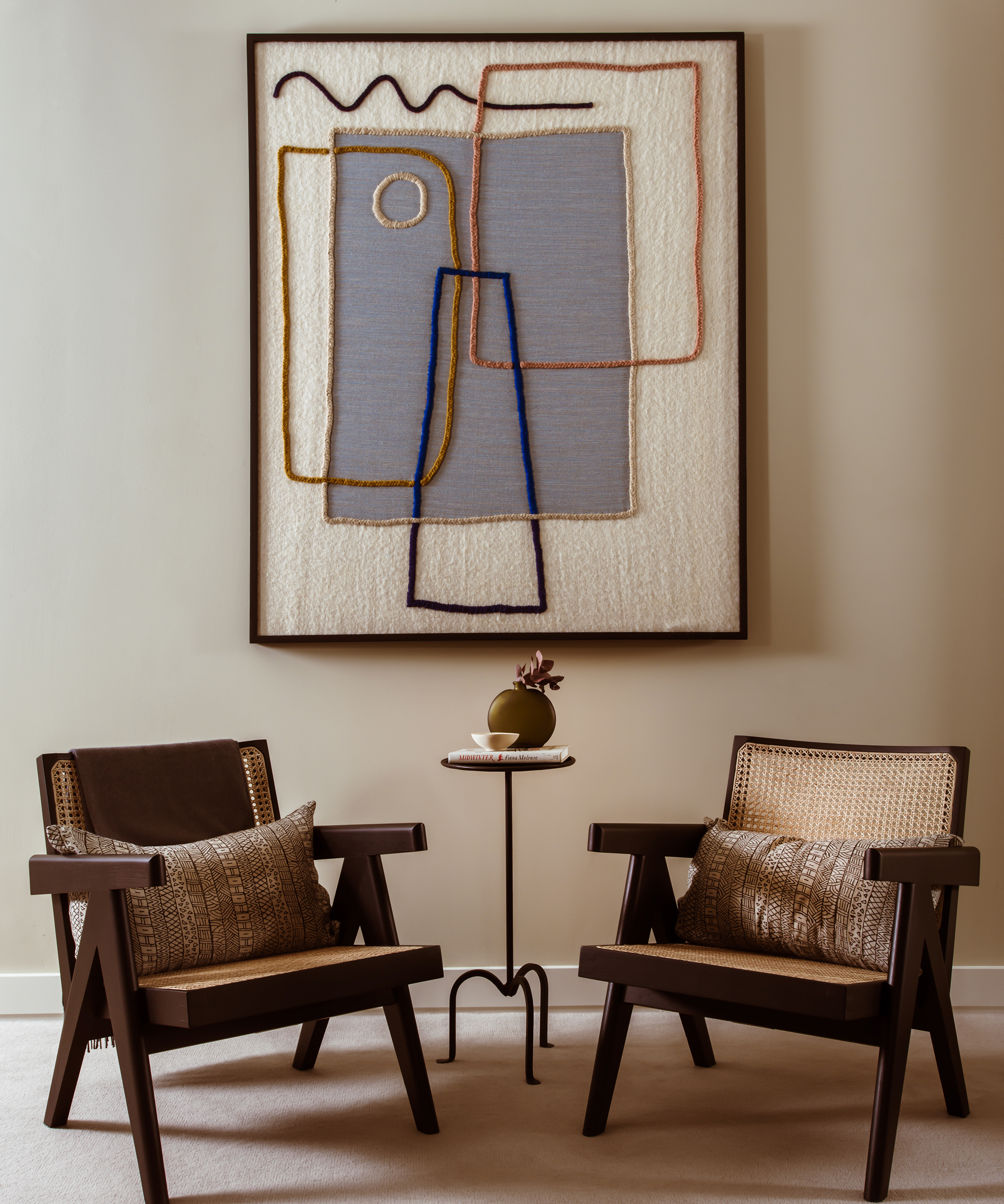 A hallway with a feature seating area, with timber and cane chairs and a textile artwork on the wall