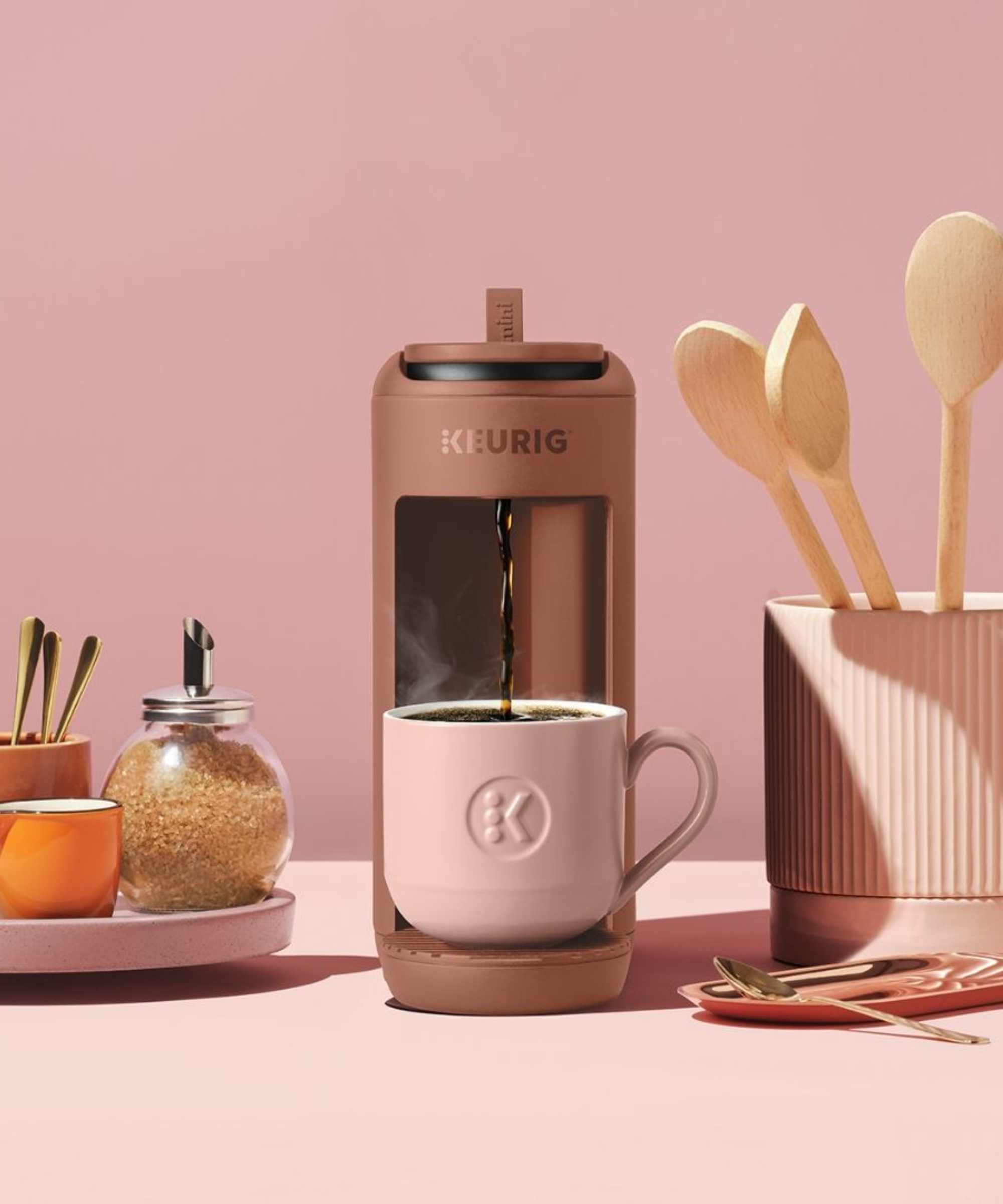 Keurig K-Mini Mate In Pink on pink counter next to pink spoon canister and coffee sugars
