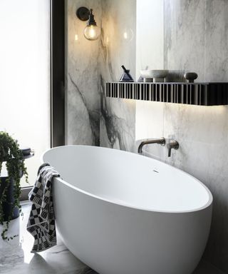 white modern bath in bathroom with black fluted shelf, large marble tiles and wall light with a pewter base, arm finished with a glass globe shade