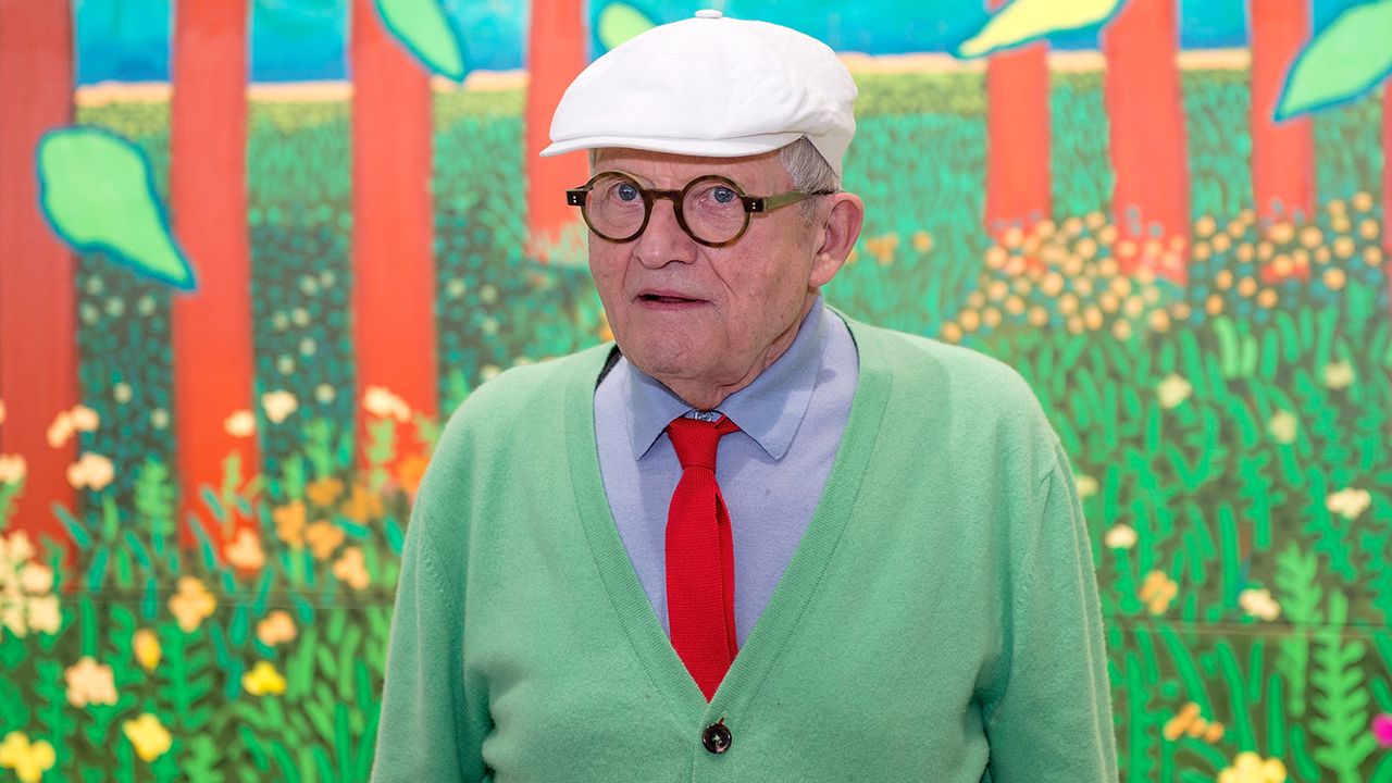 David Hockney poses in front of his painting &amp;#039;The Arrival Of Spring&amp;#039; in 2017 