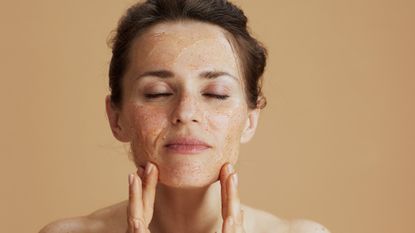 Woman with hair scraped back into a bun massaging the best exfoliator into her skin - best exfoliator