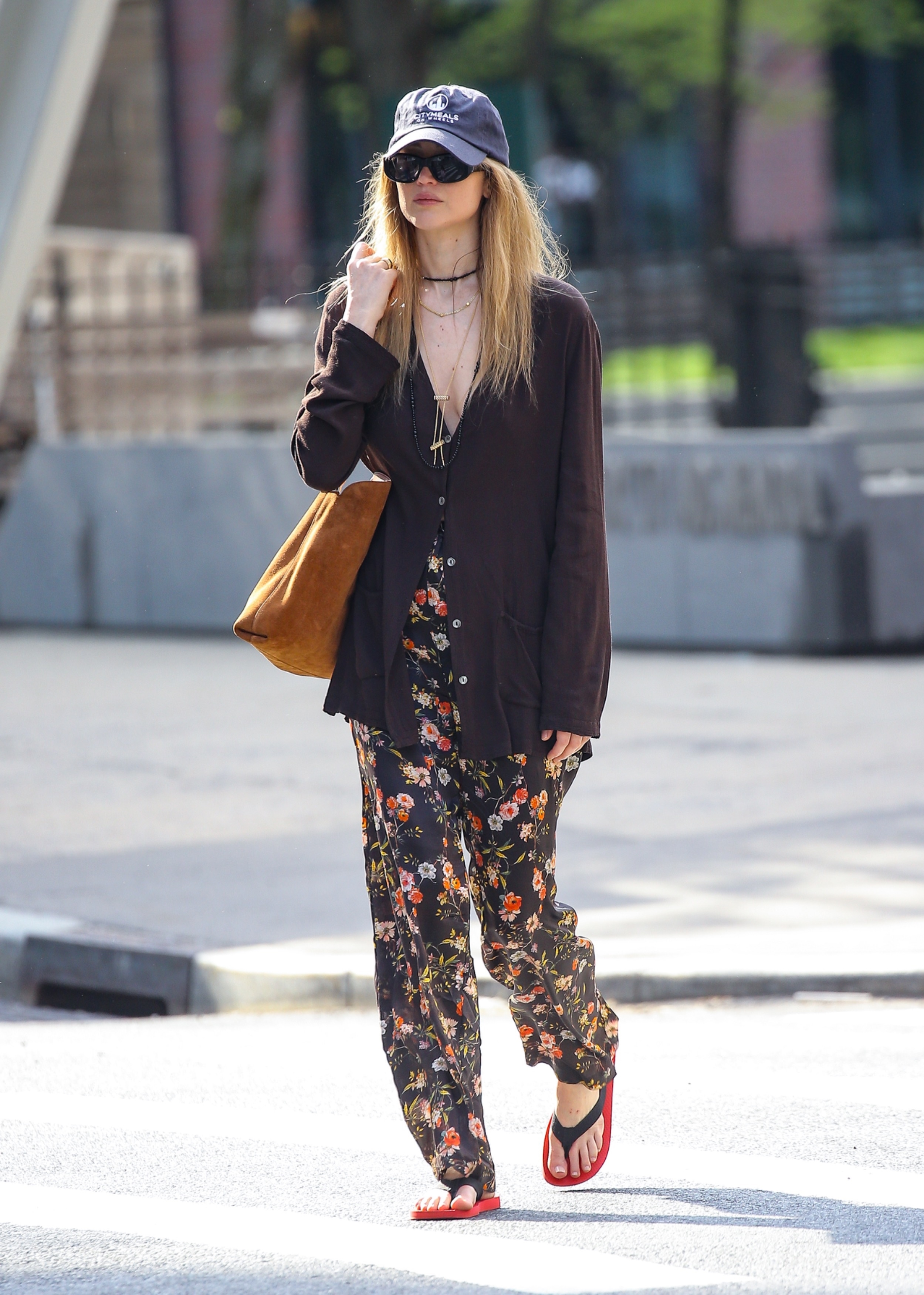Jennifer Lawrence walks outside in New York wearing floral trousers with The Row black and red flip flops and a brown suede tote bag.