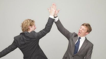 Two men in suits high five.