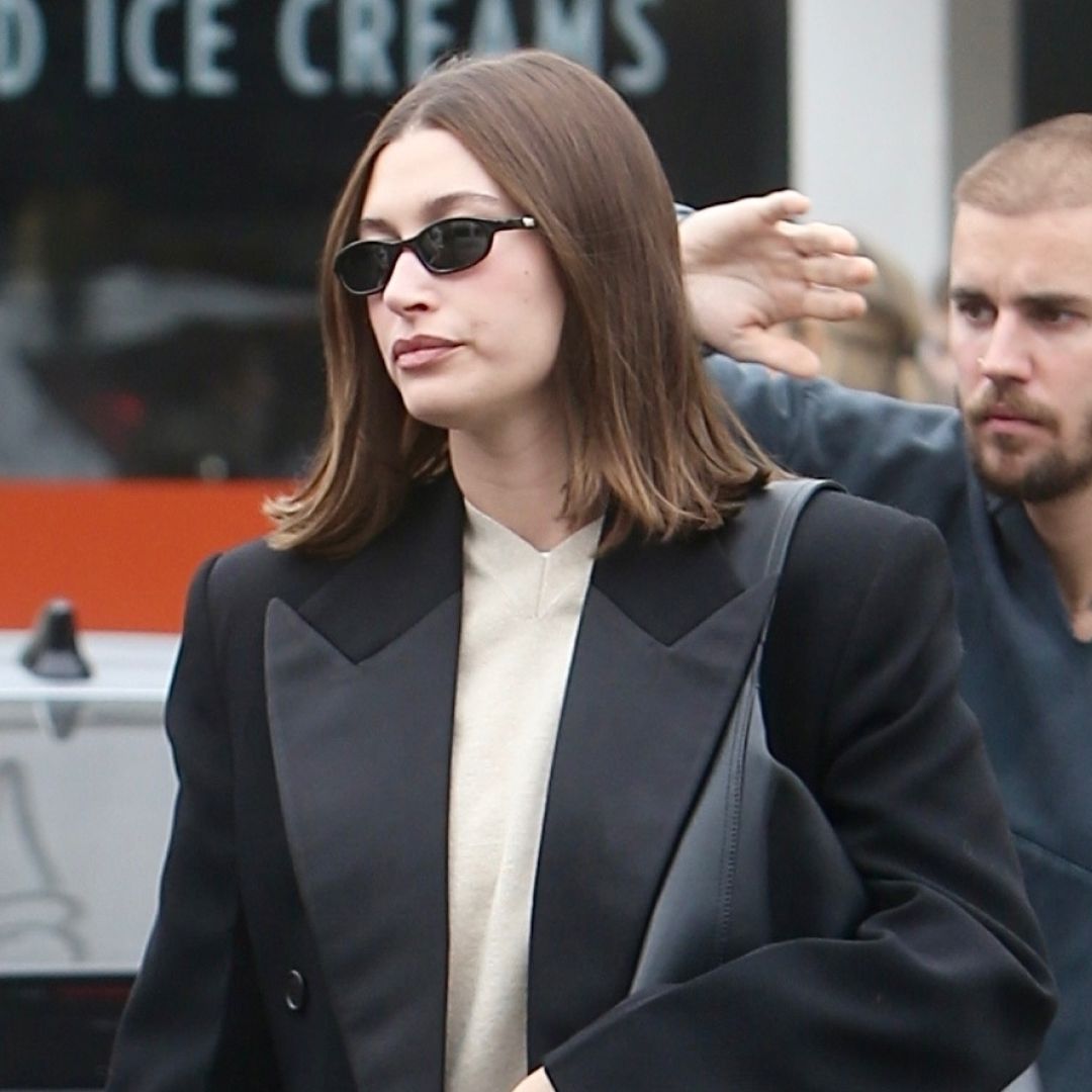 Hailey Bieber wears gray sweatpants and black slippers with a long winter coat and carries a black leather oversize bag as she grabs lunch with husband Justin Bieber
