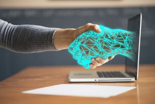A human hand shakes a digital hand coming out of the screen of a laptop in this illustration of AI assisting a human.