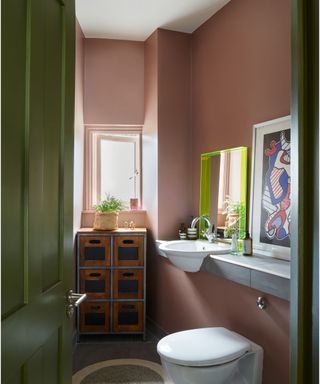 small bathroom with dark pink walls, green door and white fixtures