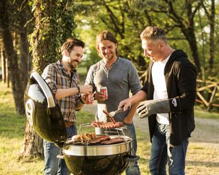 three male friends standing around a grill