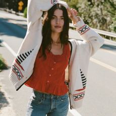 Young brunette woman wearing Abercrombie knitted cardigan, blue jeans, and red top, stood at road side.