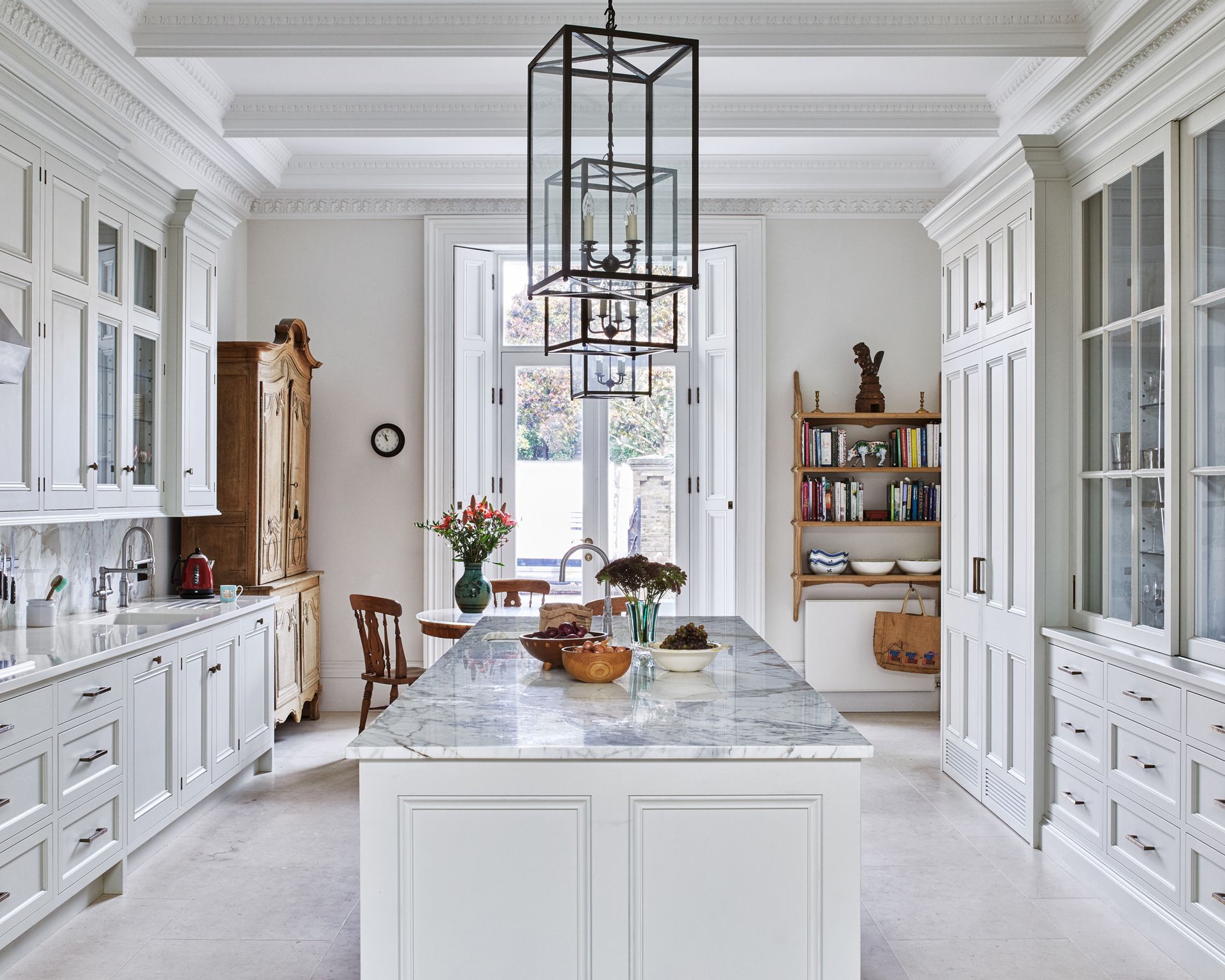 A kitchen with white cabinets and a marble topped island, with natural stone floor tiles