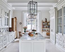 A kitchen with white cabinets and a marble topped island, with natural stone floor tiles